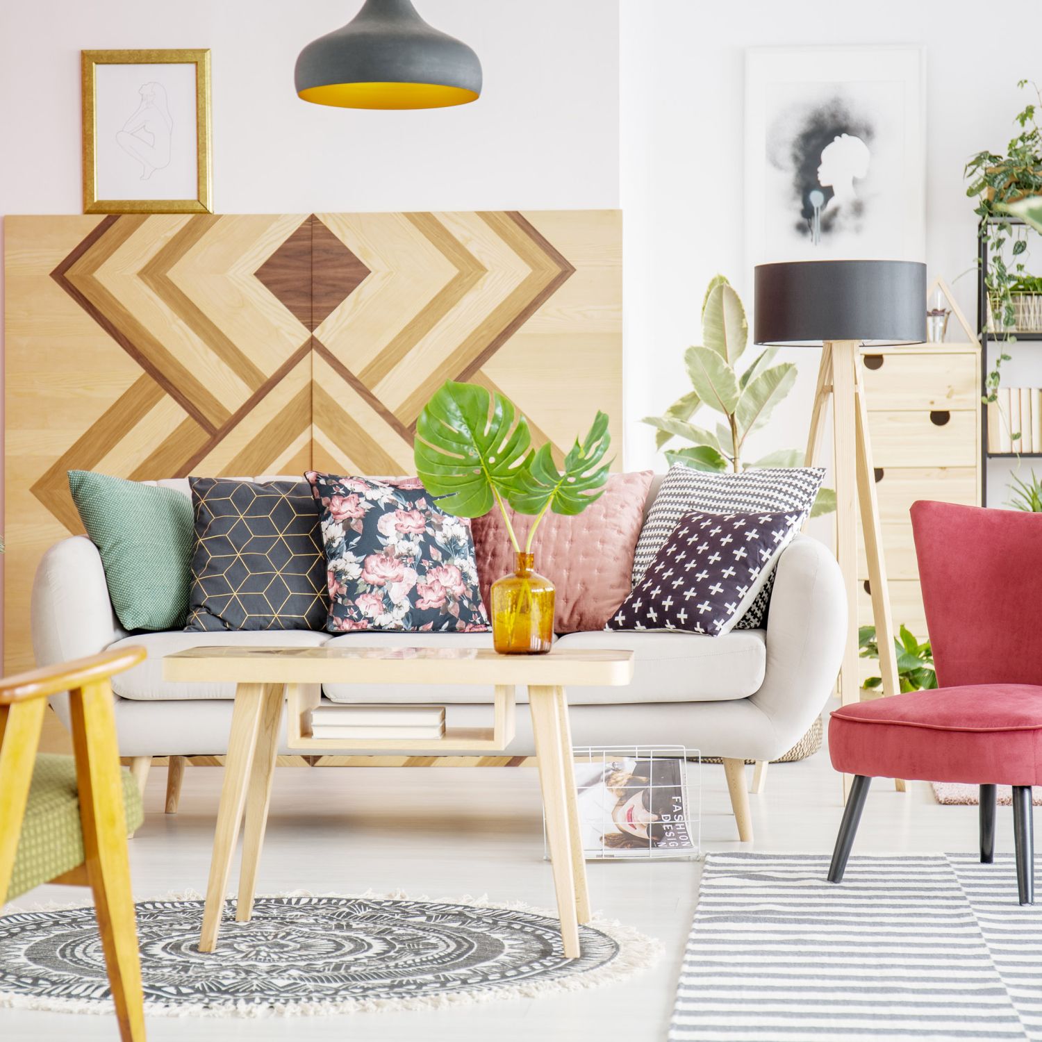 Patterned pillows on sofa next to red armchair in cozy living room interior with wooden furniture.