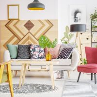 Patterned pillows on sofa next to red armchair in cozy living room interior with wooden furniture.