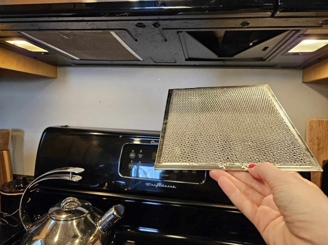 Removing the range vent filter for cleaning in the kitchen.