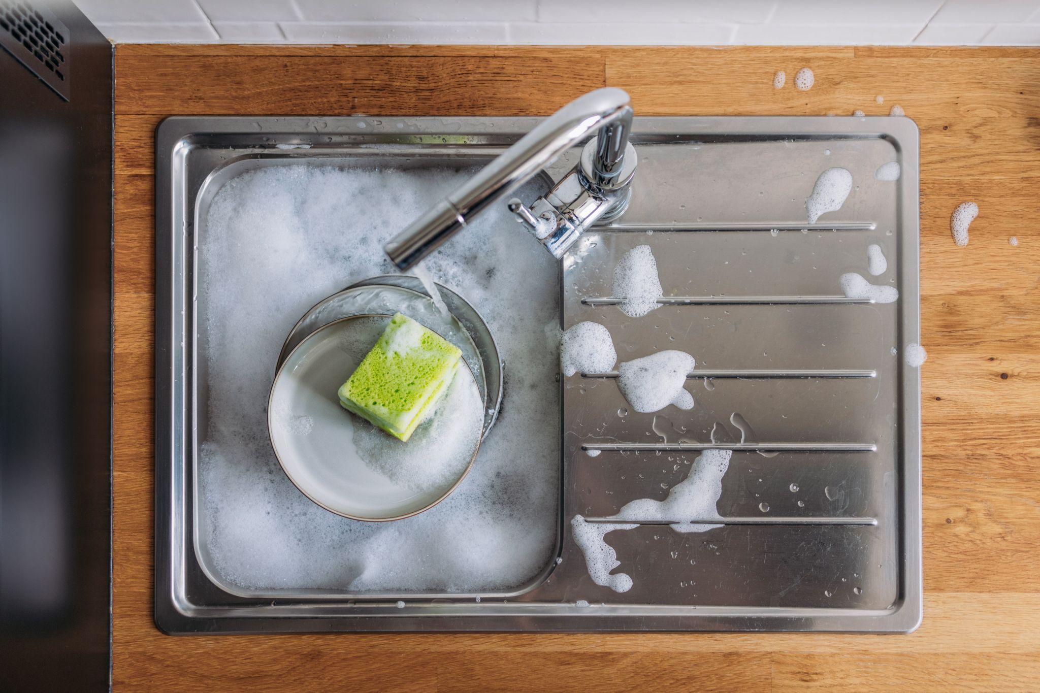 Overhead shot of sponge in a soapy sink. Things you need to clean in the kitchen and bathroom.