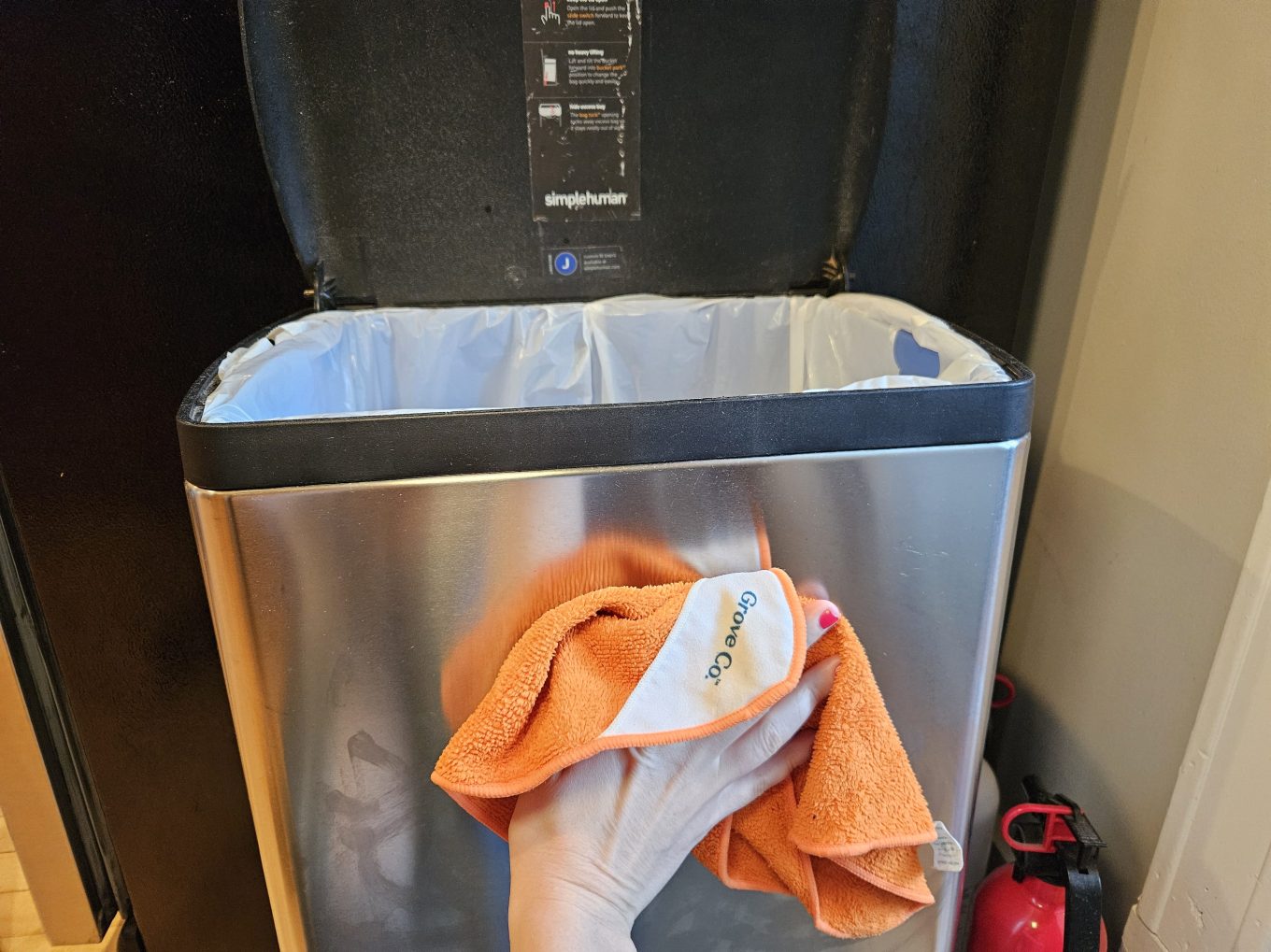 A person cleaning the outside of a stainless steel trashcan.