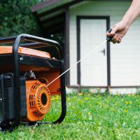 A portable electric generator being started by hand.