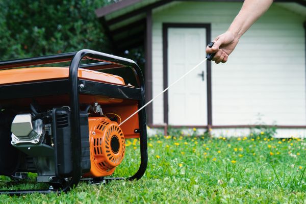 A portable electric generator being started by hand.