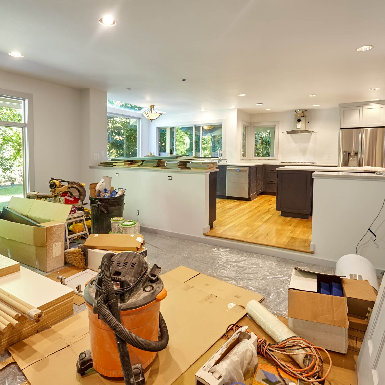 A living room and dining room full of renovation supplies including fresh flooring, new drywall, a new door and more.