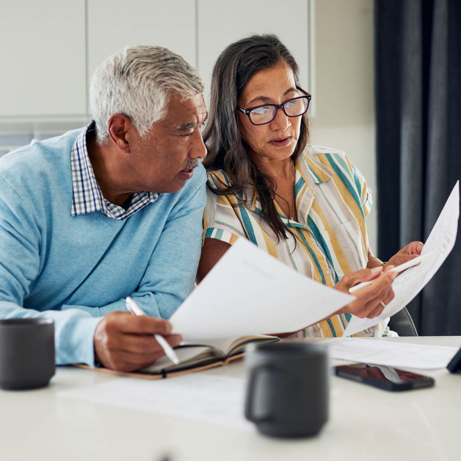 An older couple is sitting at their kitchen table reviewing financial documents.