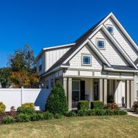 The front view of a new construction cottage craftsman style white house with a triple pitched roof with a sidewalk, landscaping and curb appeal.