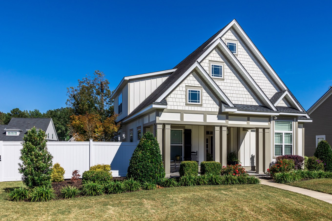 The front view of a new construction cottage craftsman style white house with a triple pitched roof with a sidewalk, landscaping and curb appeal.
