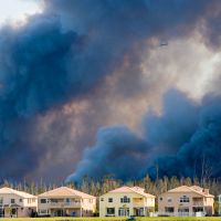 Smoke billowing from a wildfire behind a row of houses, contributing to unhealthy air quality.
