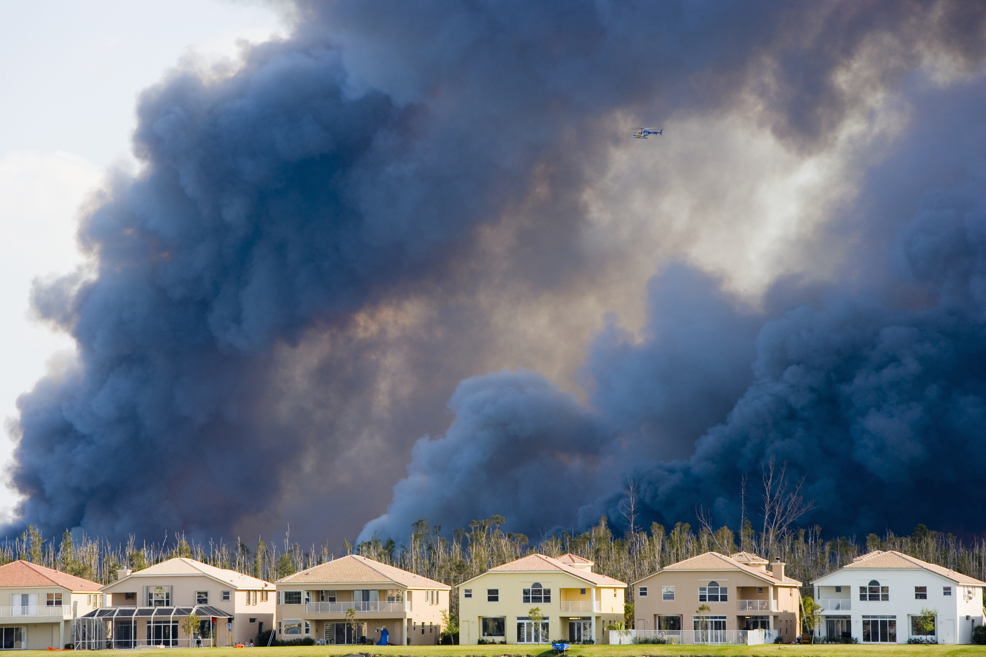Smoke billowing from a wildfire behind a row of houses, contributing to unhealthy air quality.