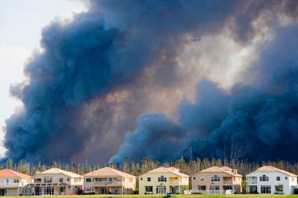 Smoke billowing from a wildfire behind a row of houses, contributing to unhealthy air quality.