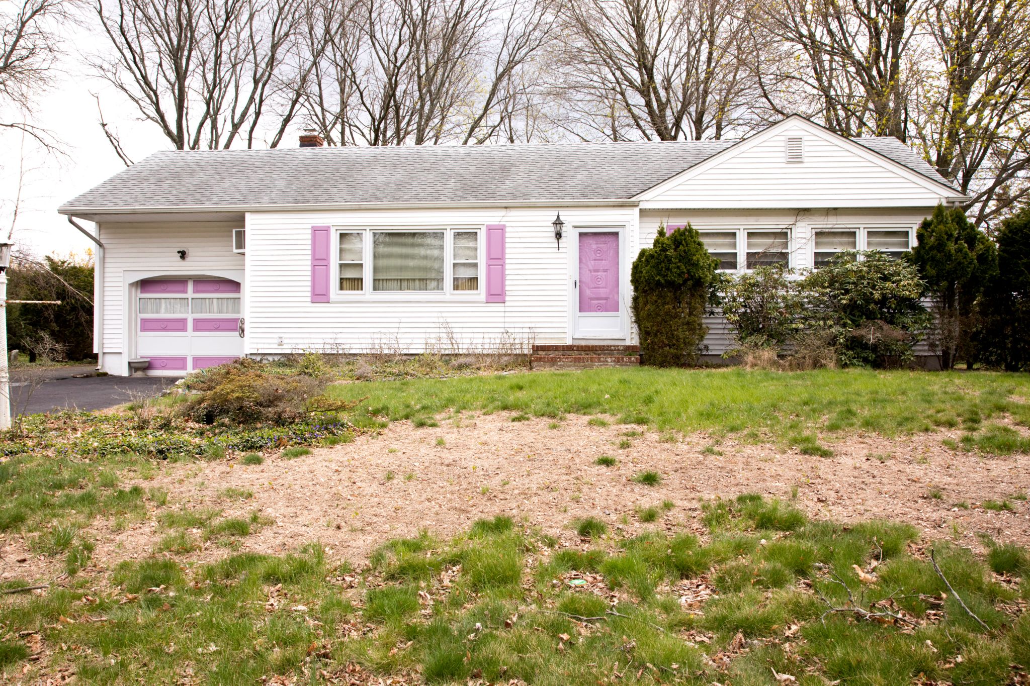 A white house with a front yard that features a lot of brown grass.