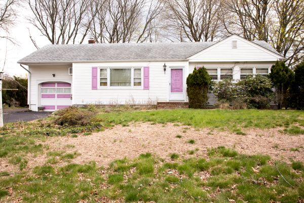 A white house with a front yard that features a lot of brown grass.