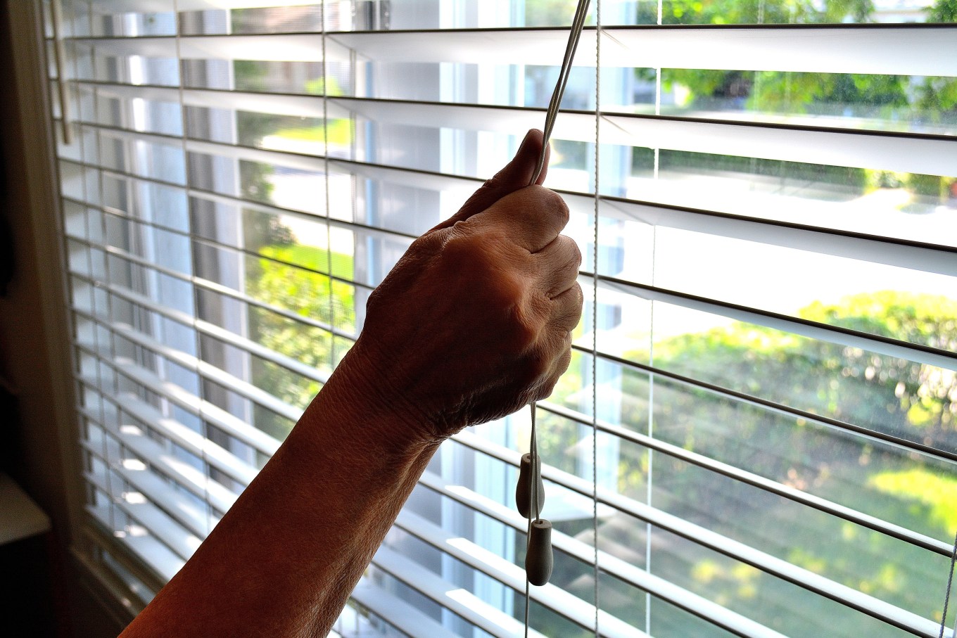 A shot of someone's arm closing a bedroom window shade.
