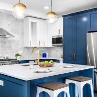 A luxurious white and blue kitchen with gold hardware, stainless steel appliances, and white marbled granite counter tops.