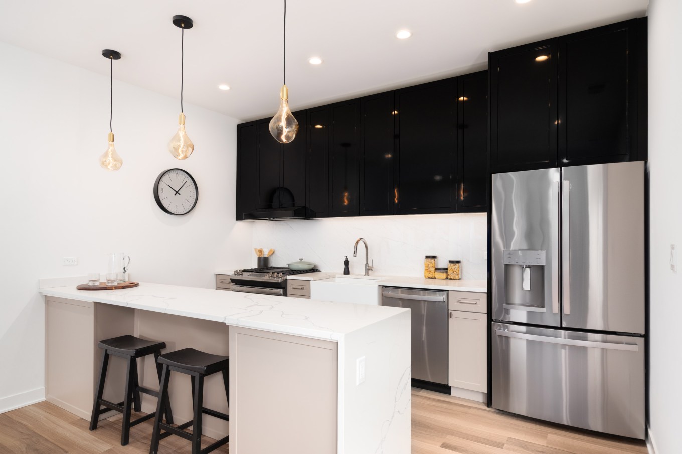 A beautiful renovated kitchen with black and brown cabinets, white granite waterfall countertops, and stainless steel appliances.