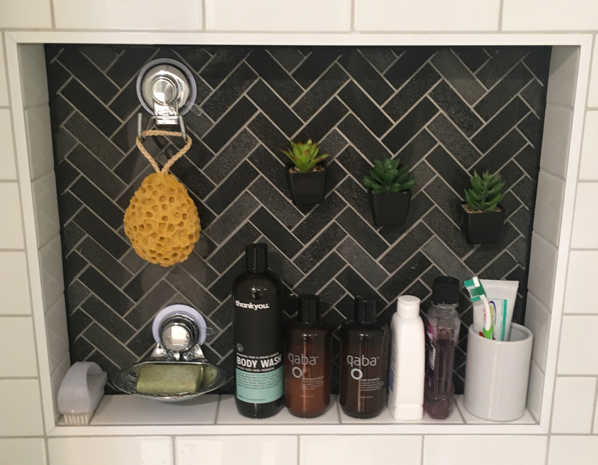 A black tiled built-in shelf in a white tiled shower