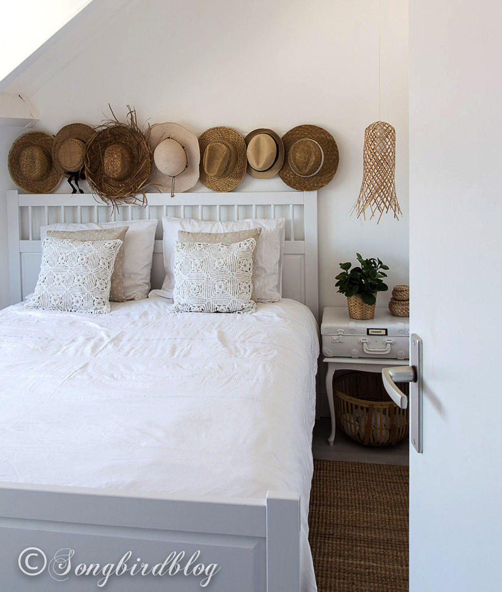 White bed with assortment of straw and cowboy hats above it