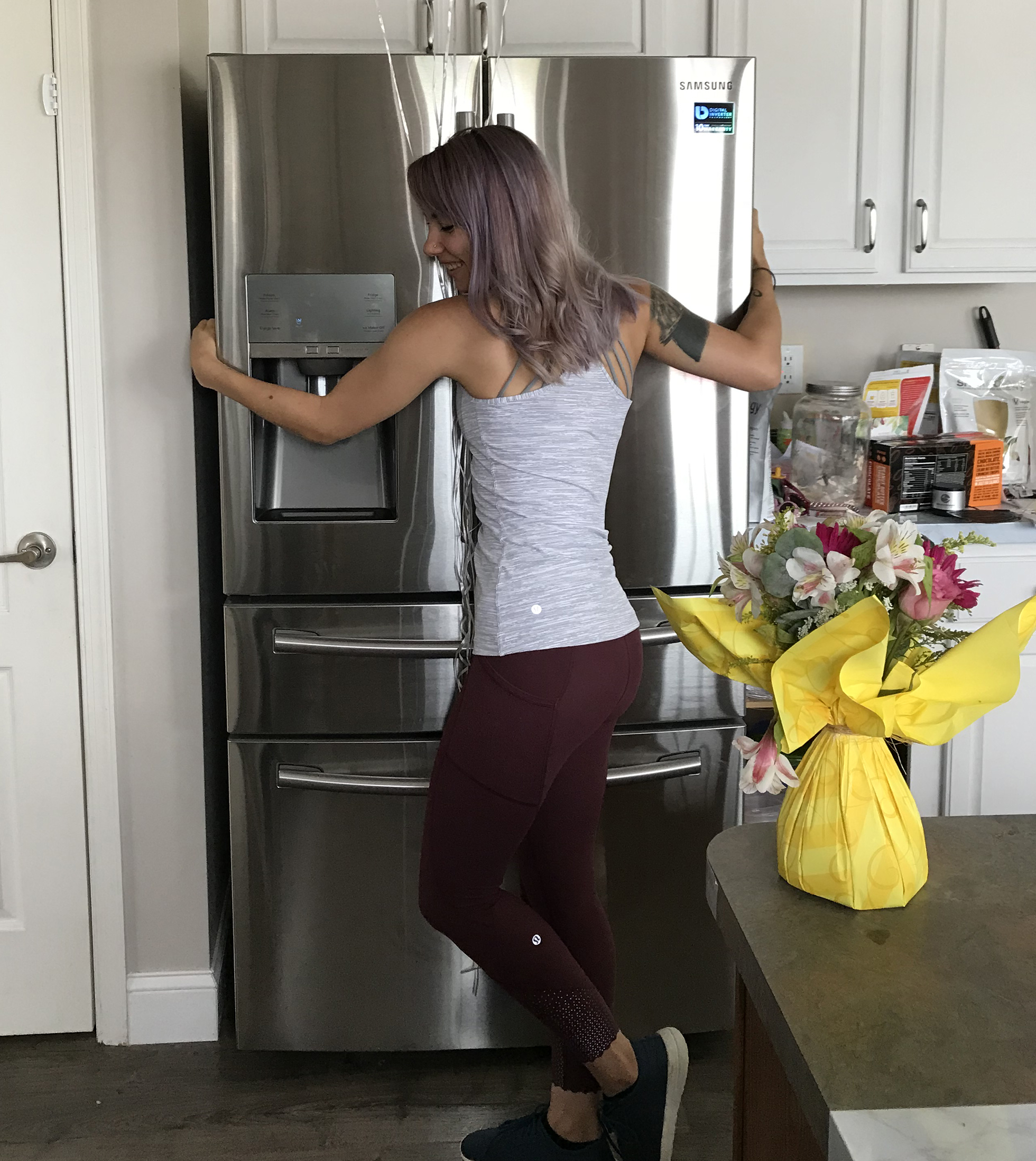 Woman in workout clothes hugging stainless steel fridge
