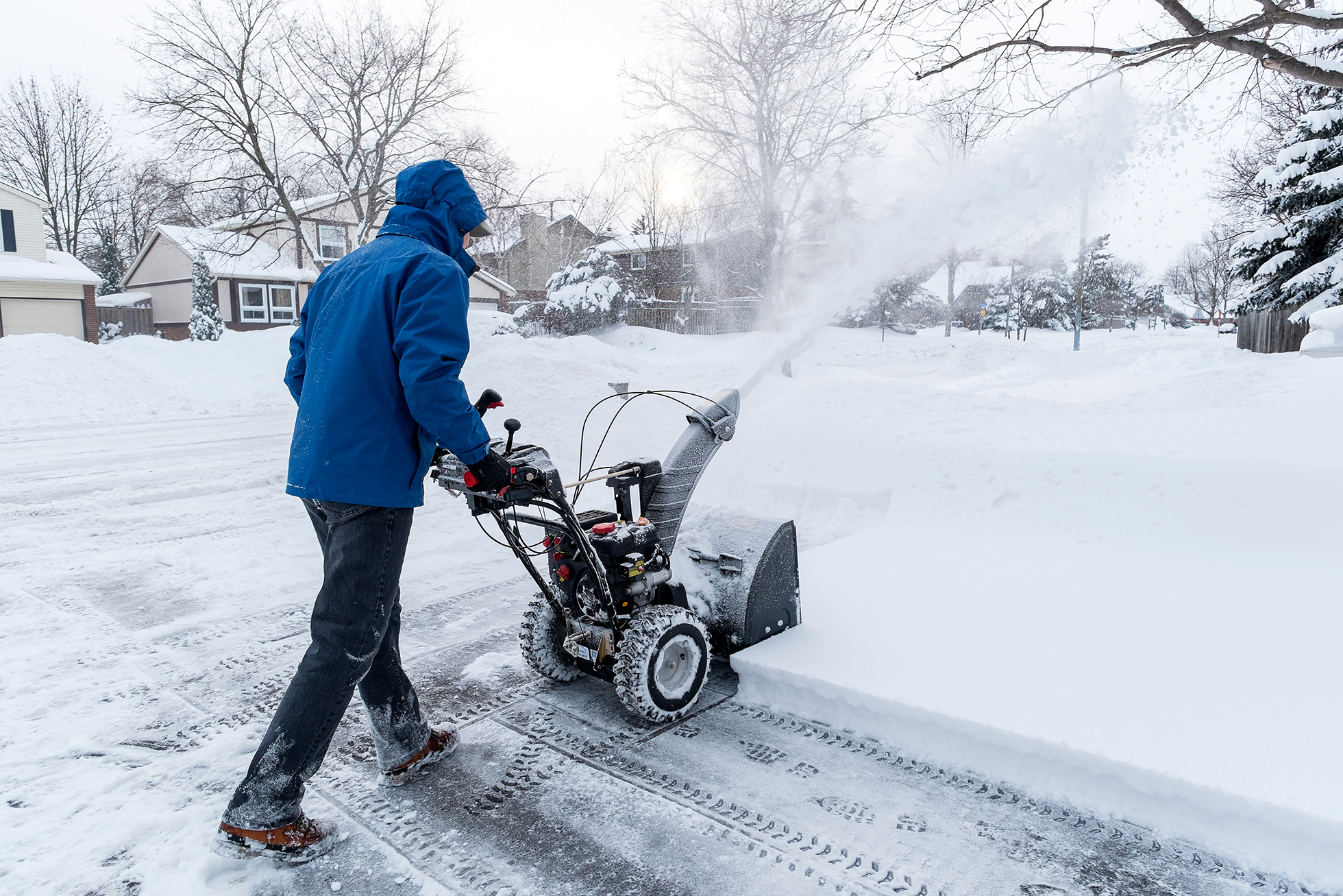 Person in blue parka using snowblower to clear sidewalk path