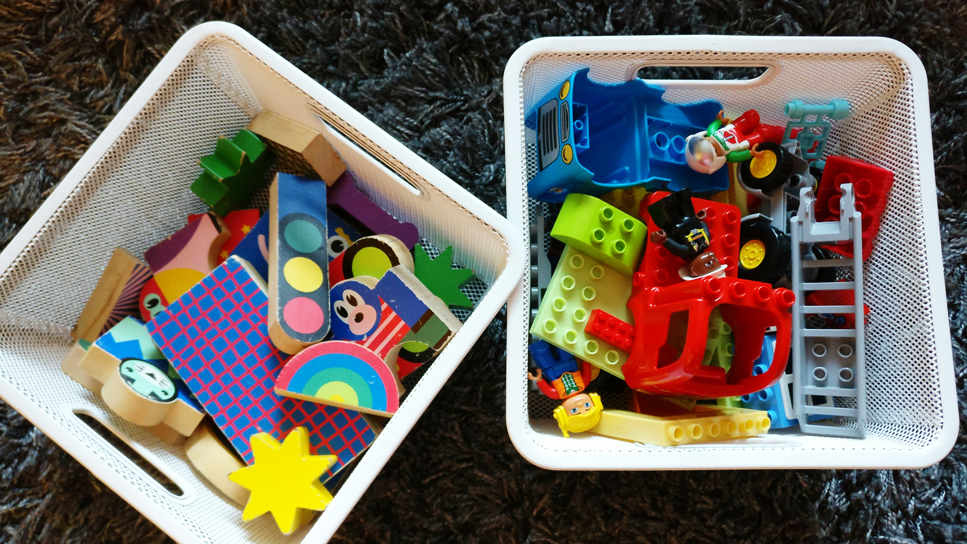 Two white square baskets full of multi-colored toys on floor