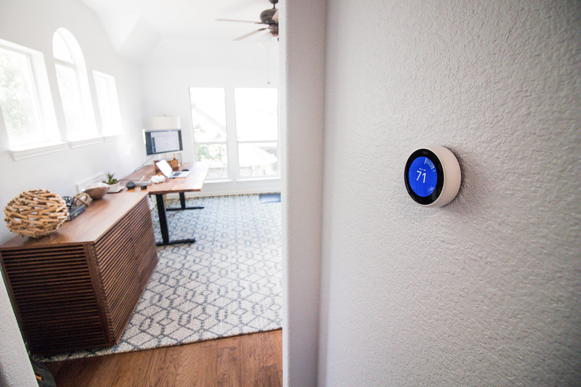 White smart thermostat on textured wall leading into office