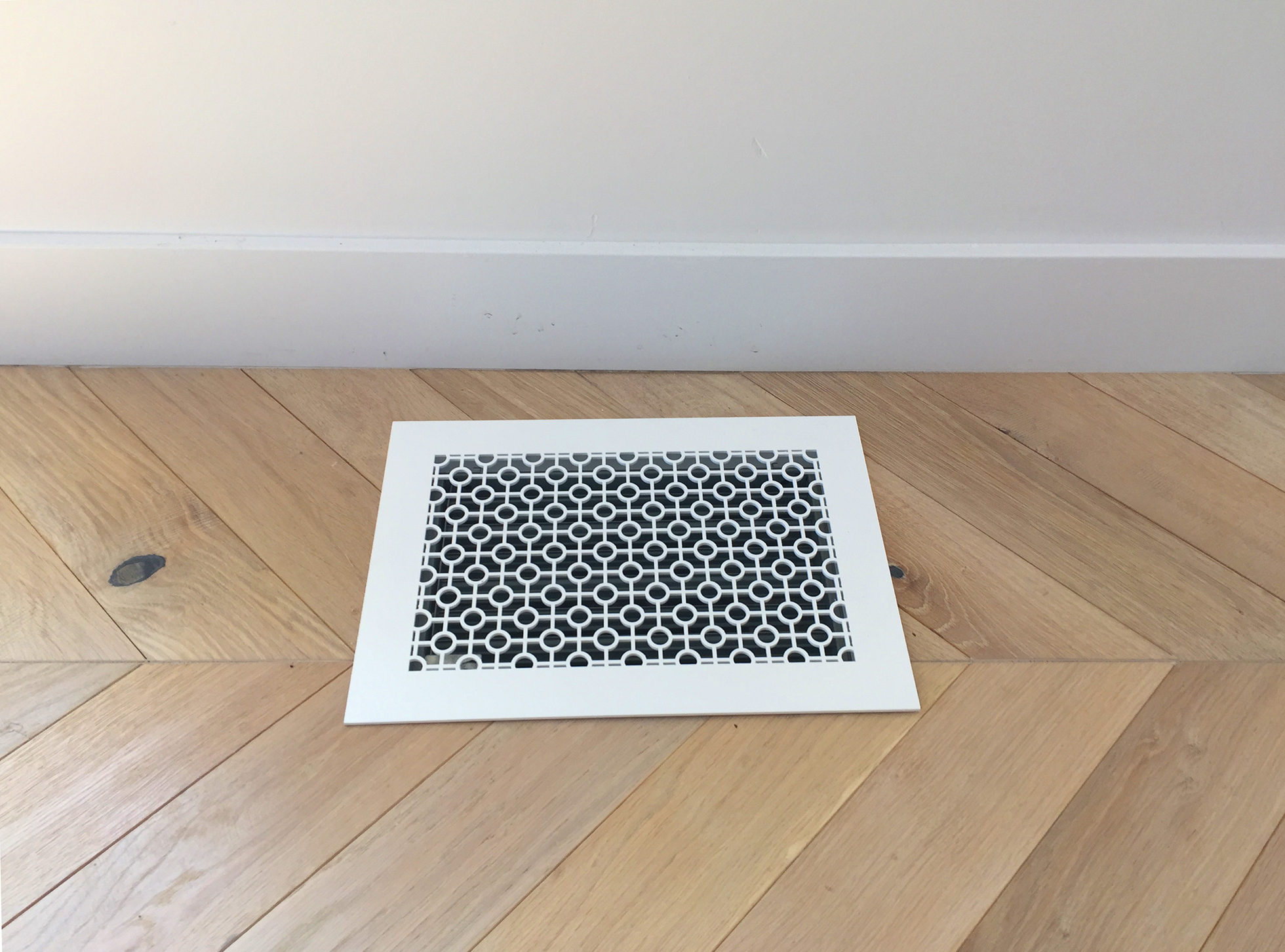 White metal floor vent in herringbone wood floor
