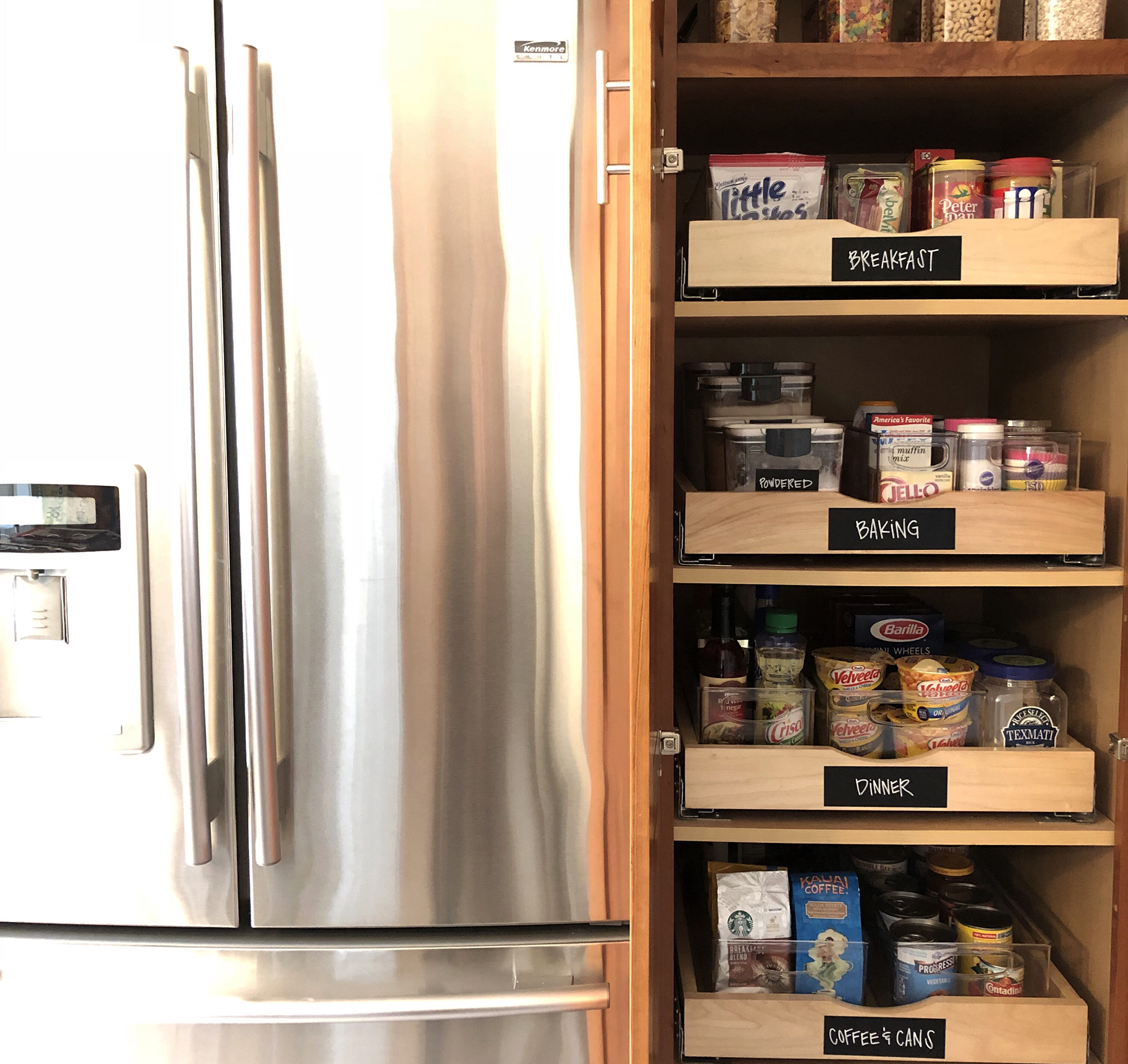 Stainless steel fridge beside cupboard with roll out drawers