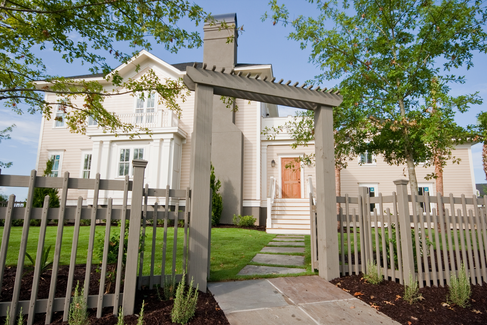A gray fence with arch in front of a white house