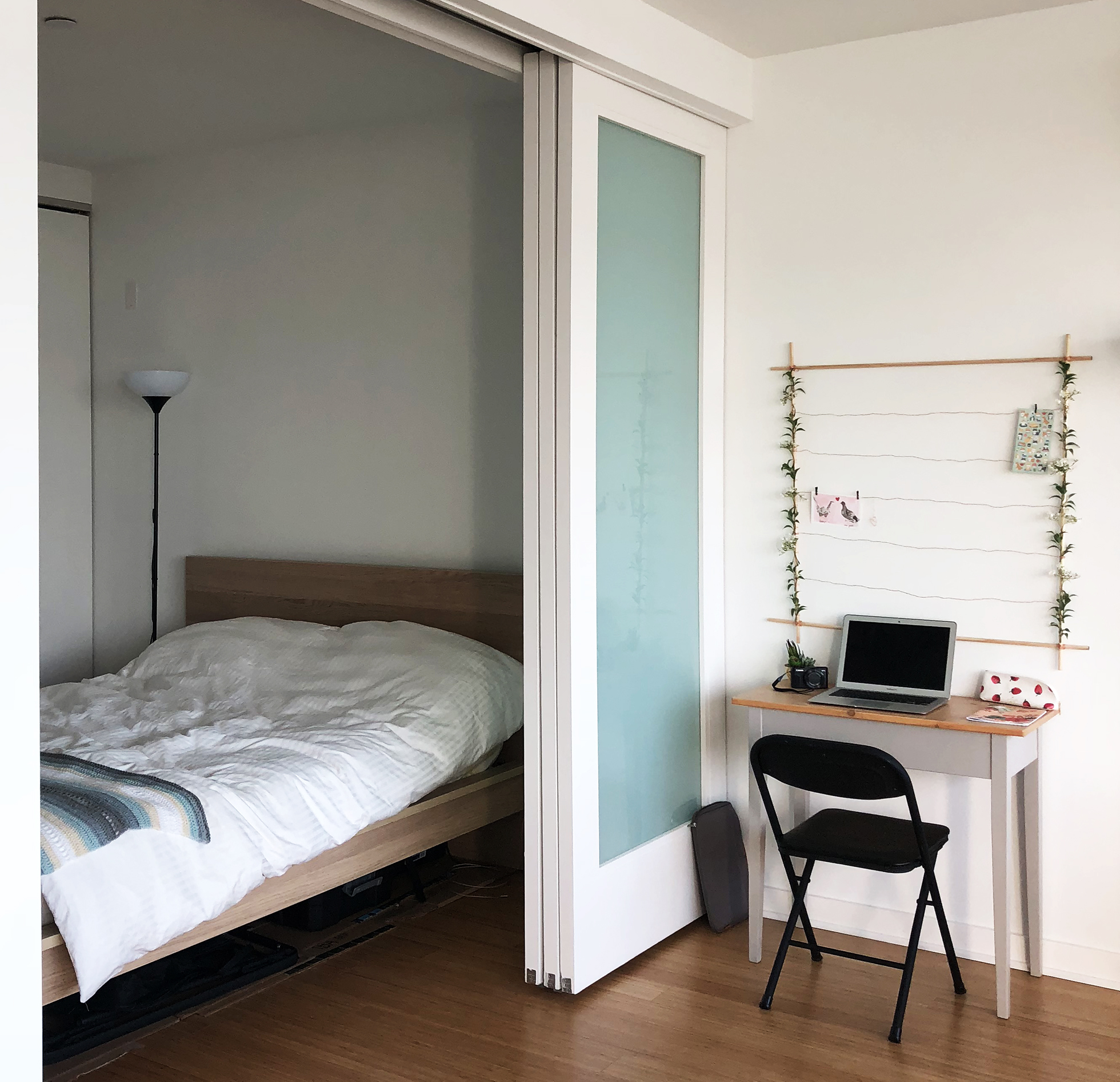 White bedroom with natural wood floor, bed frame, and desk