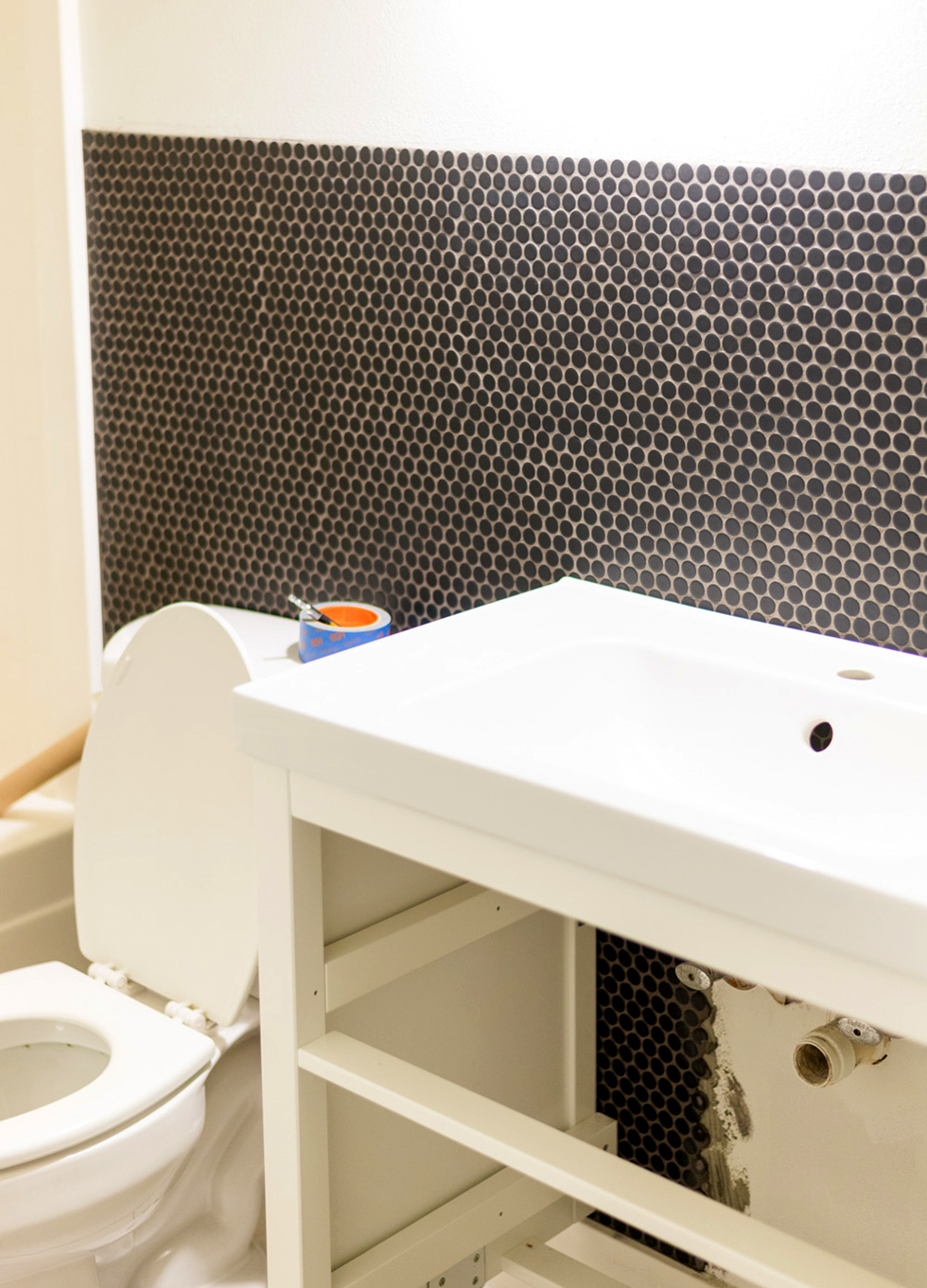 White bathroom wall being laid with black penny tile