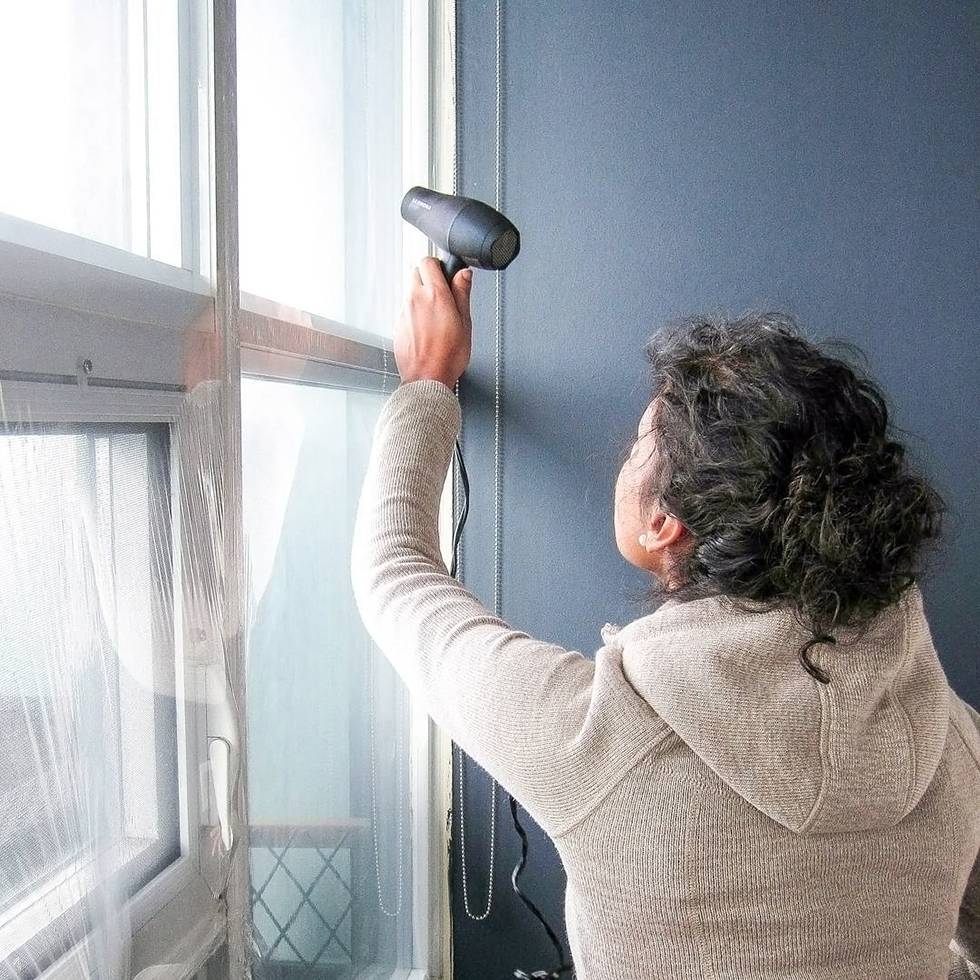Woman using hair dryer to install insulation film on window