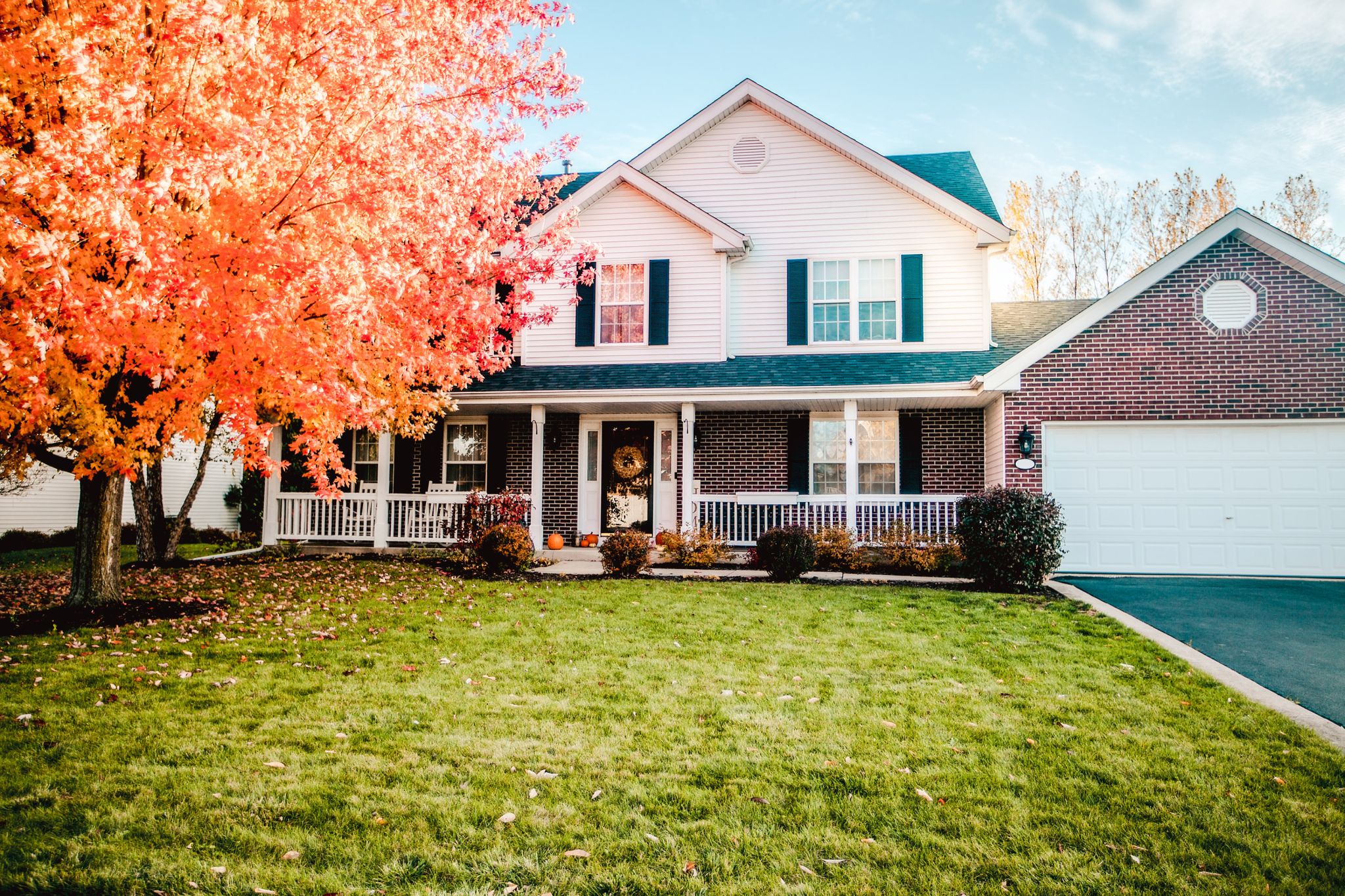 A beautiful house with a tree changing colors for Fall in front of it.