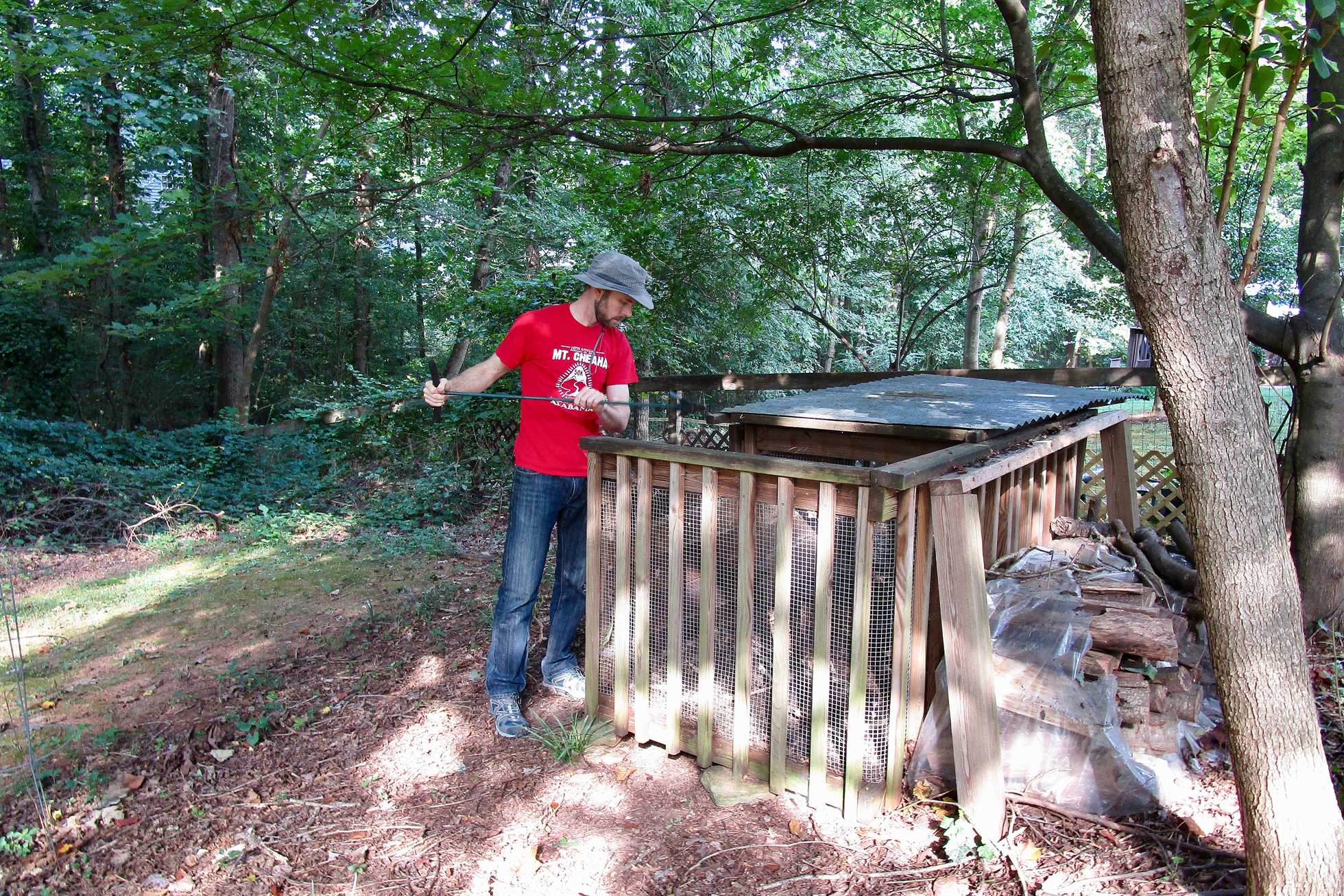 A man in a red shirt is opening a compost bin