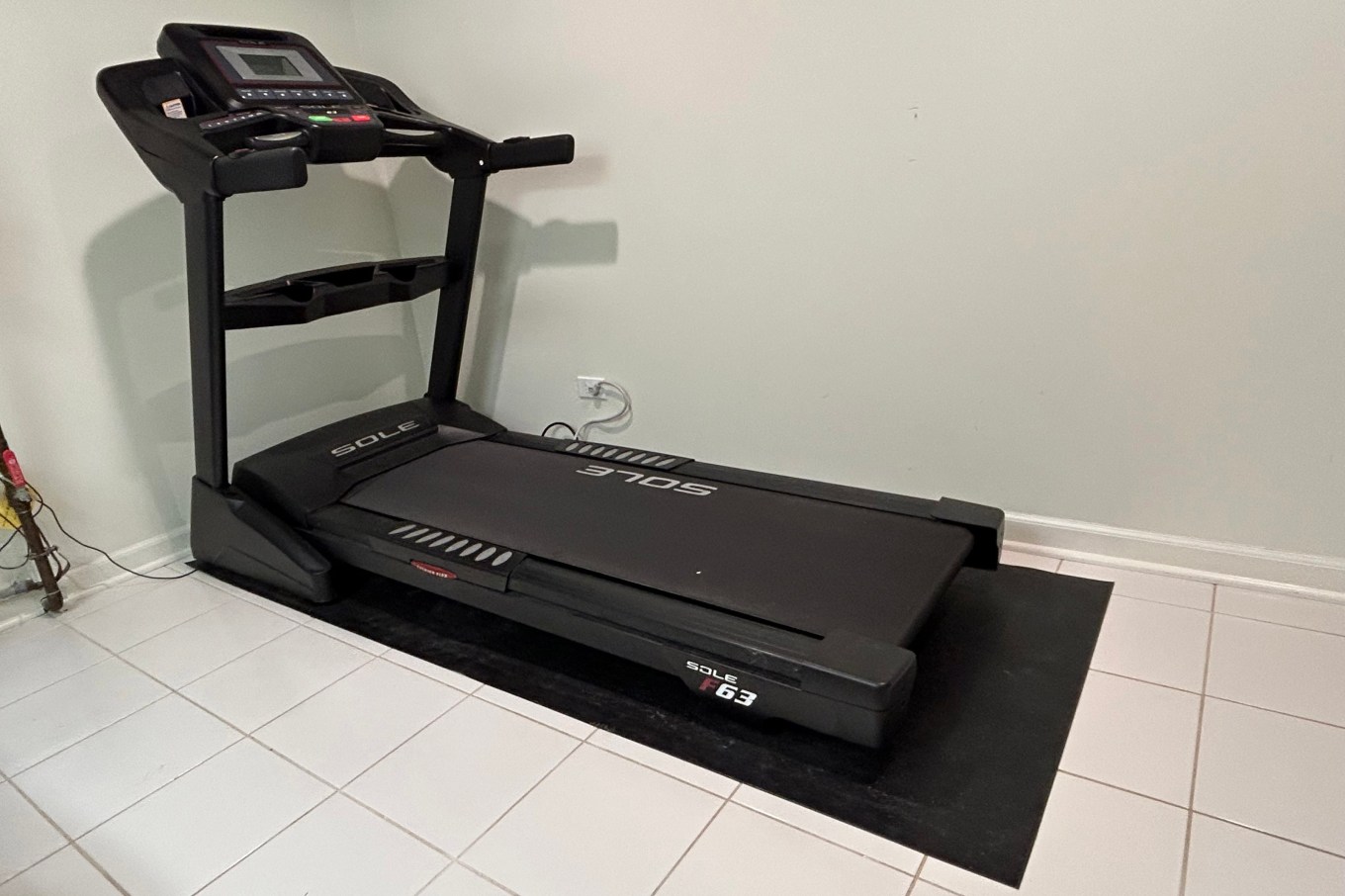 A black treadmill on a white tiled floor; an example of a hard-to-discard item.