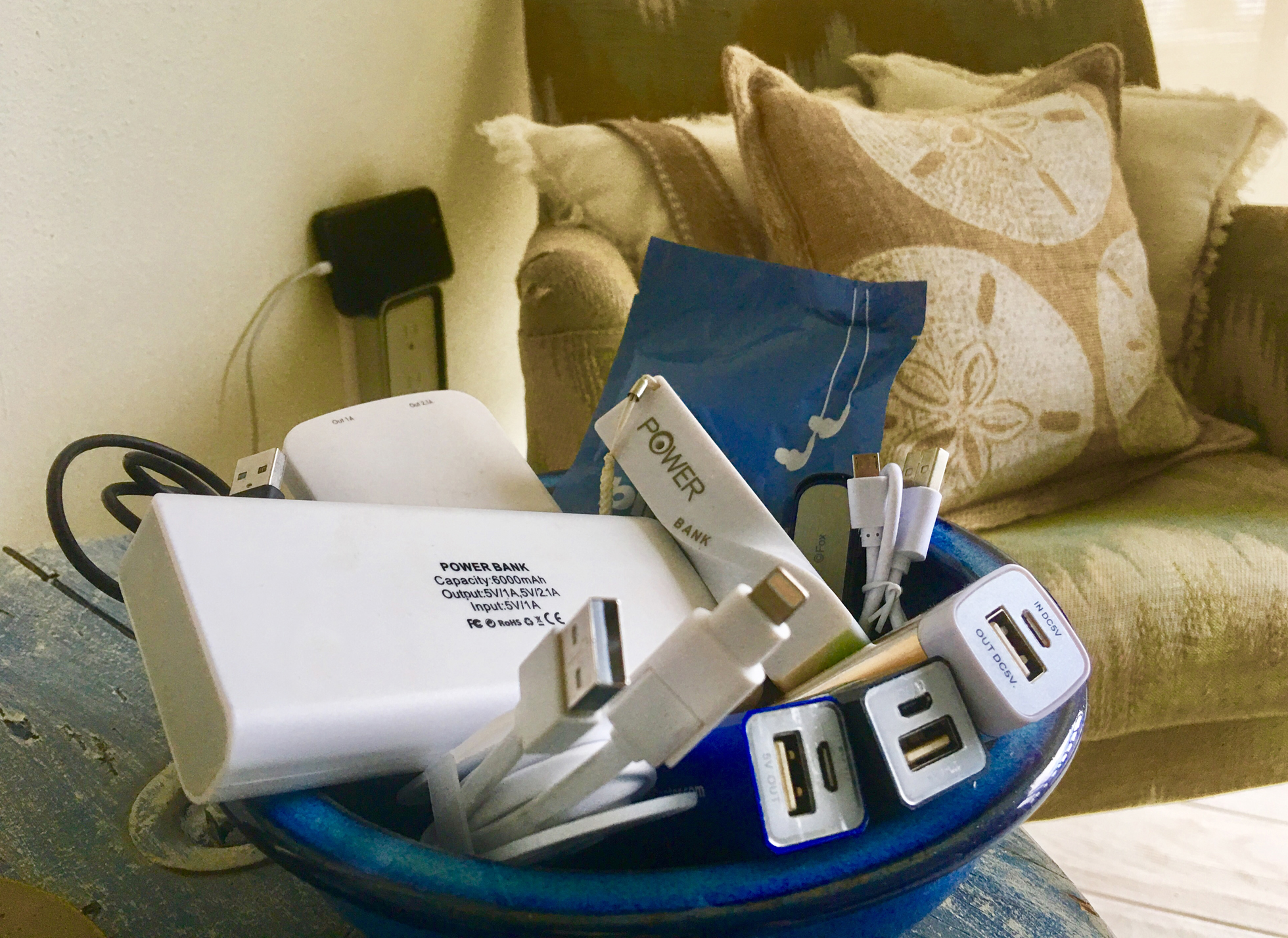 A blue bowl of white cords and chargers on a wood table