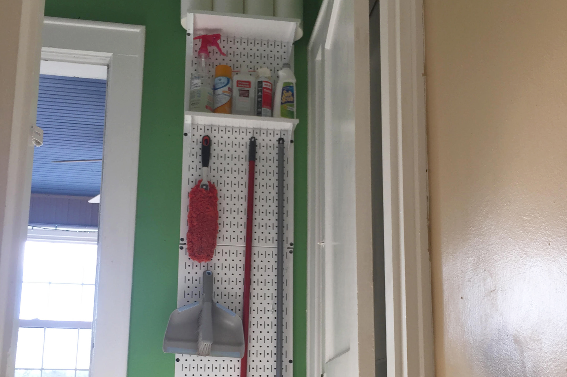 Pegboard with cleaning supplies in front of green wall