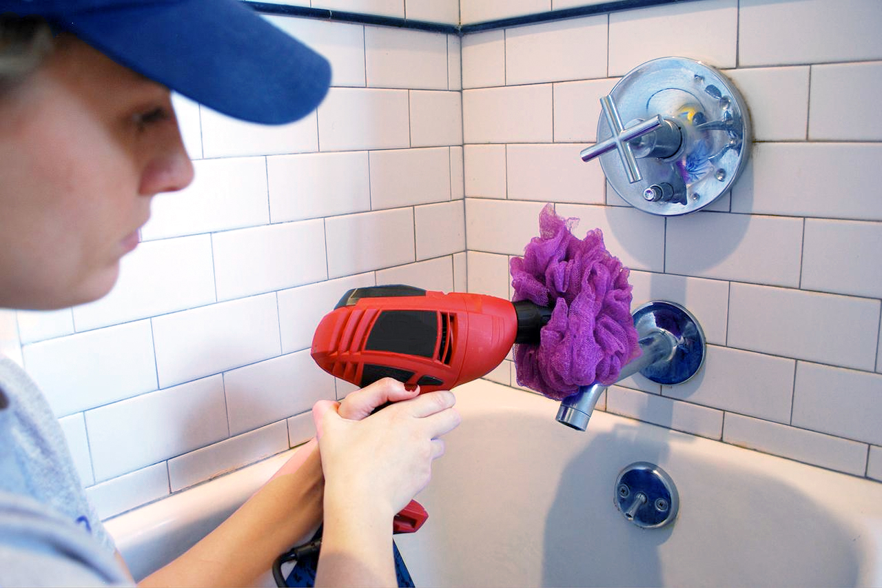 Cleaning a bathtub with a loofah attached to a drill