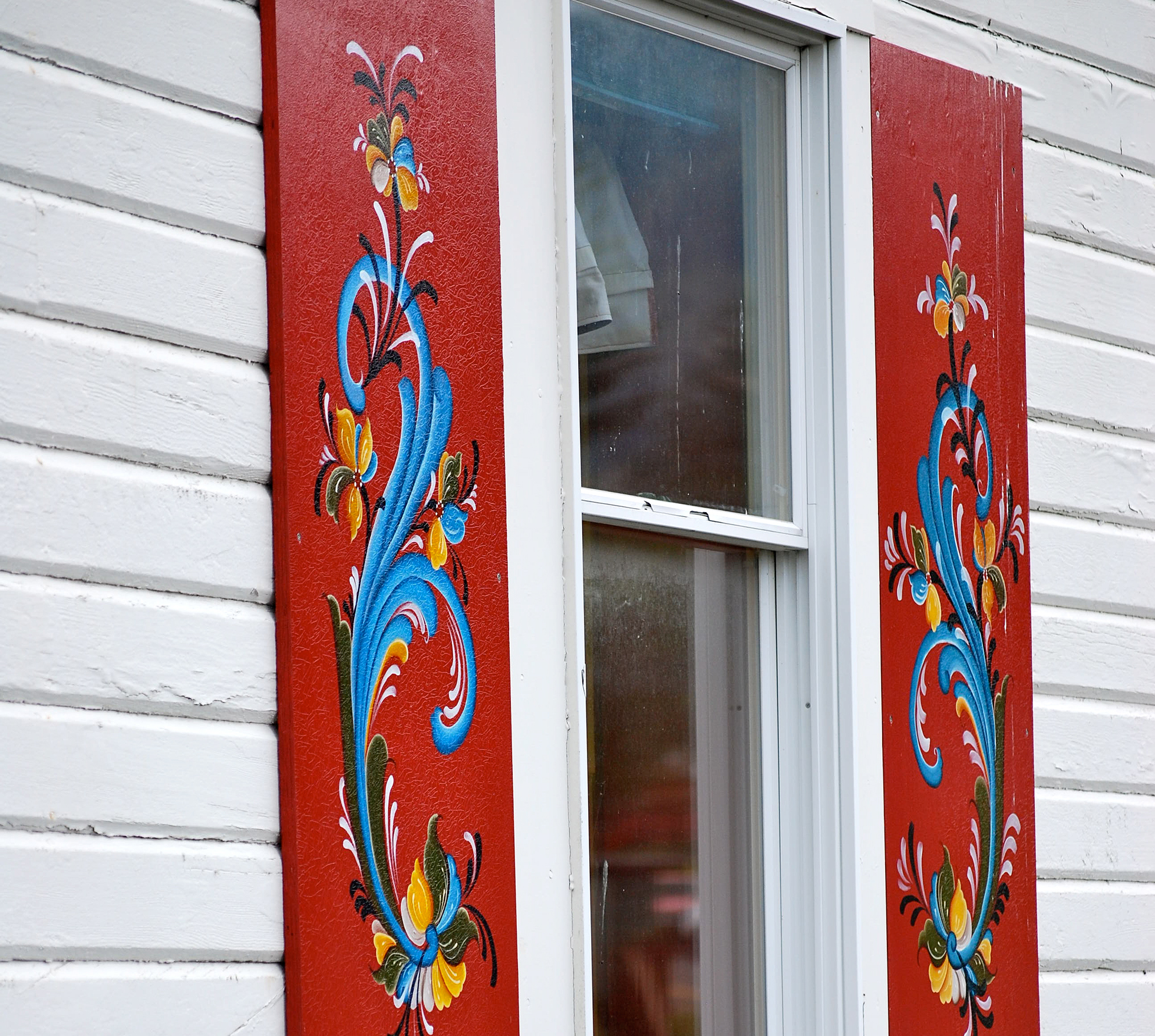 A white house with red painted shutters with rosemaling