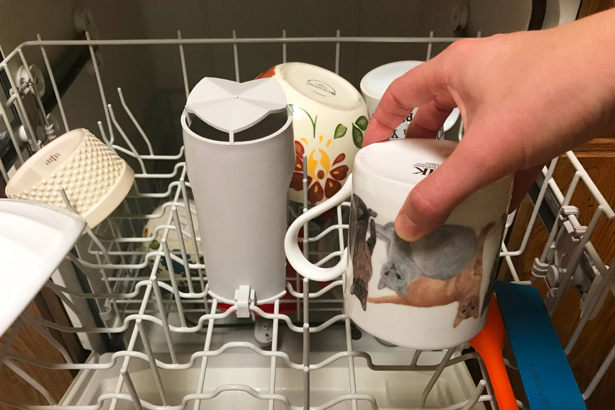 A hand putting a cat mug in a dishwasher