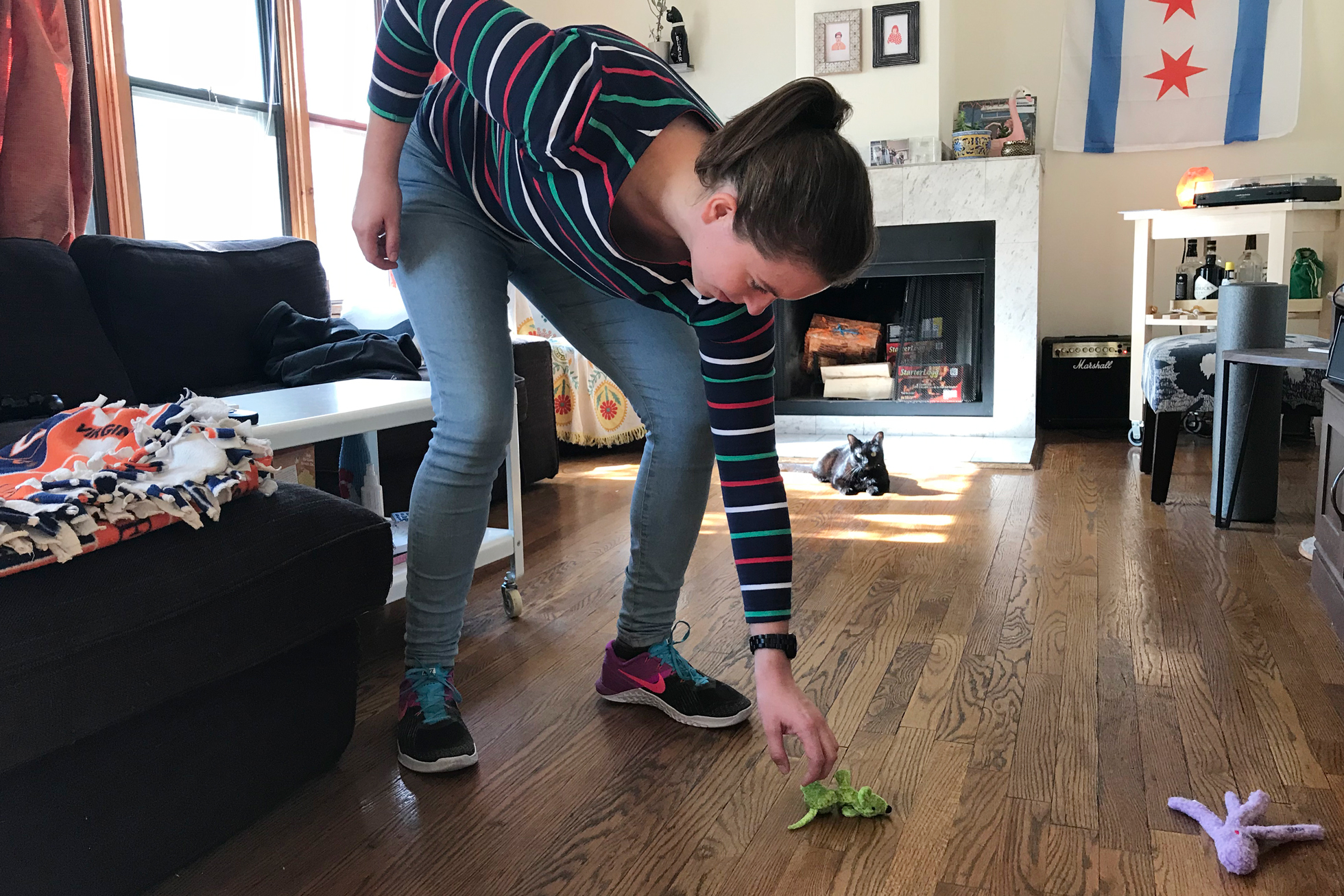 A woman picking up a green cat toy off the wood floor