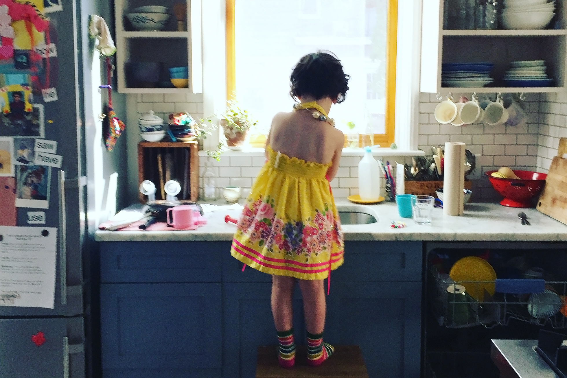 A young girl standing on a step stool in a kitchen