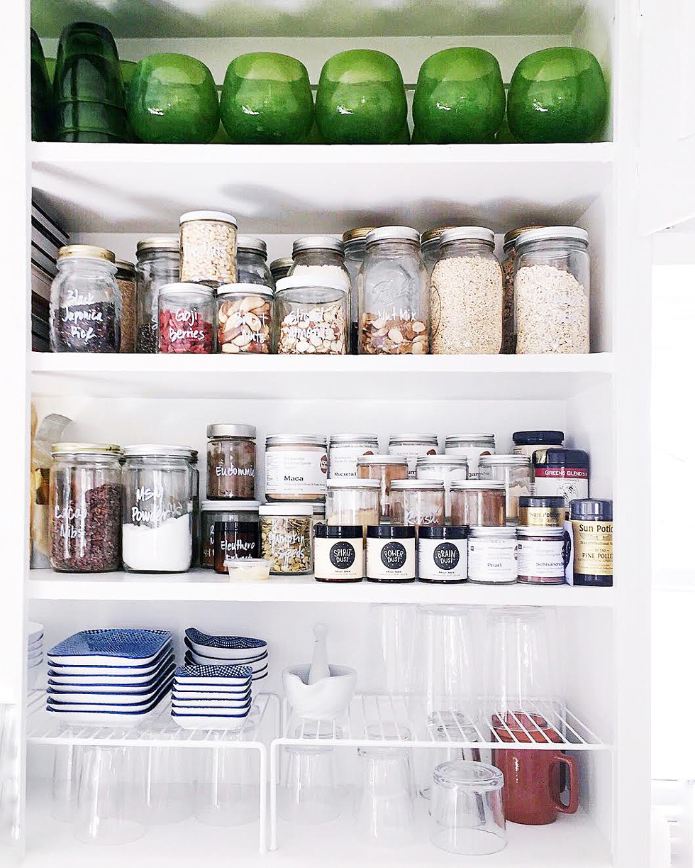 A white kitchen cupboard with green glasses and jars