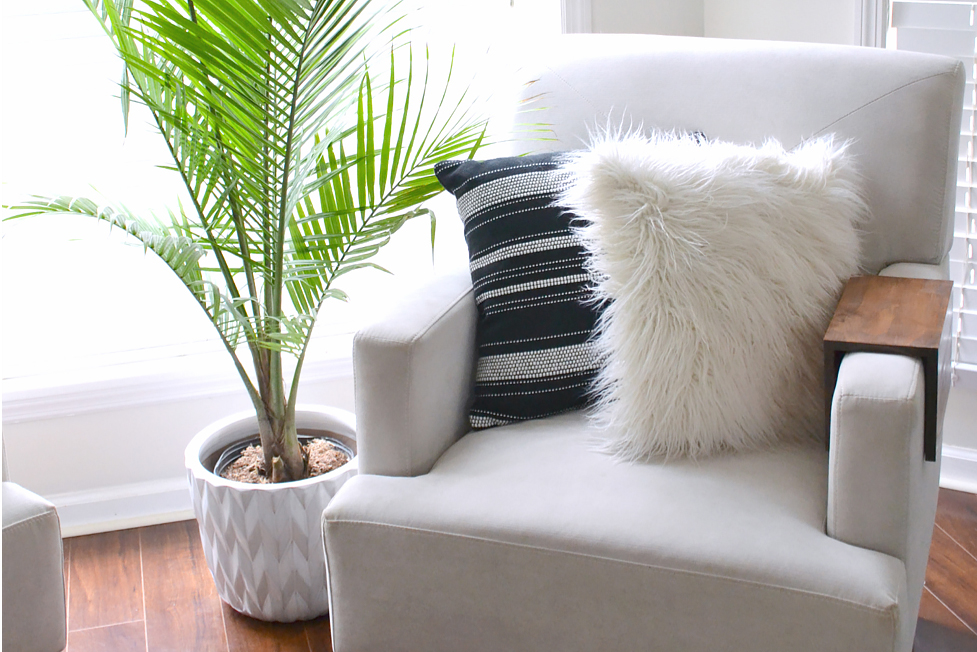 A cream-colored chair in a bright corner with a plant
