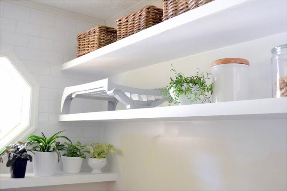A white laundry room with green plants on floating shelves