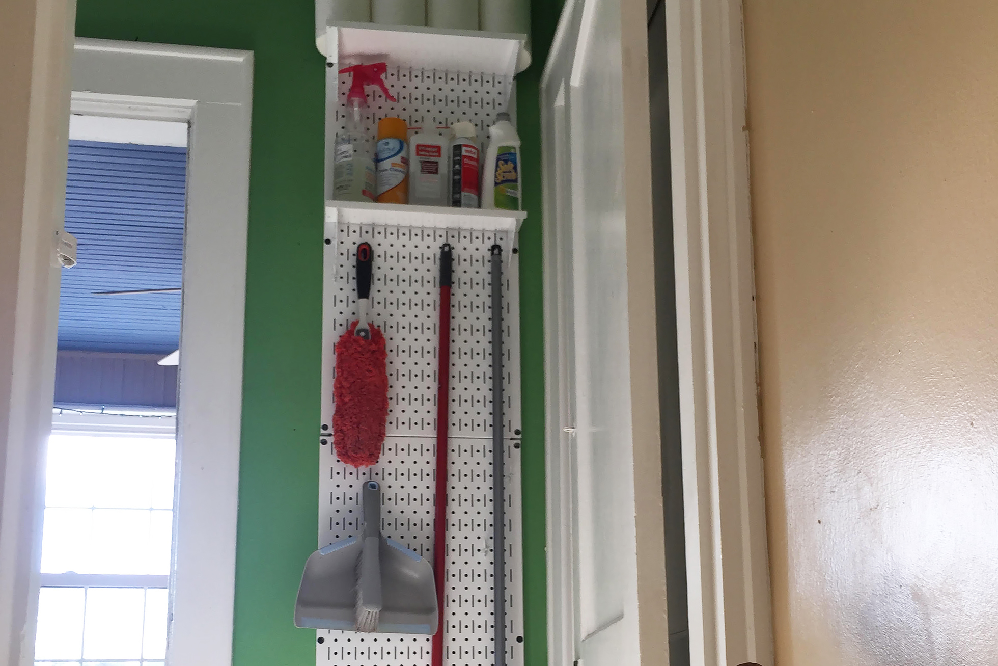 Pegboard with cleaning supplies in front of green wall
