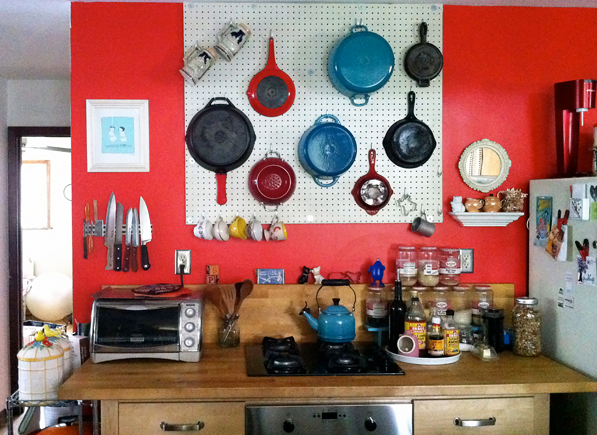 Red pegboard wall in a kitchen with pots and pans
