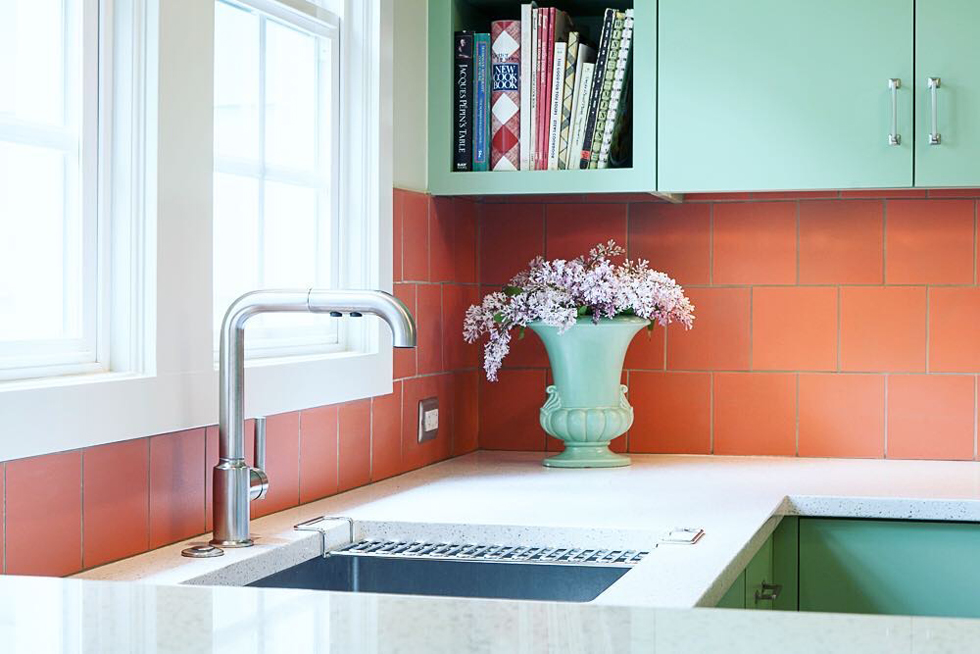 A bright poppy-colored kitchen backsplash with teal cabinets