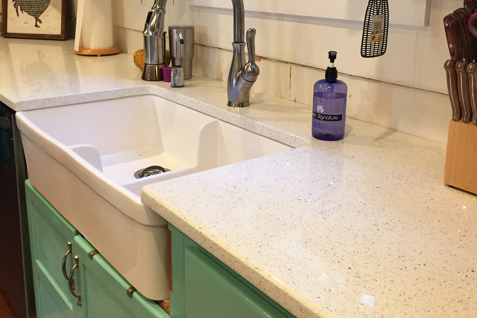 A white farmhouse sink, quartz countertop, & green cabinets