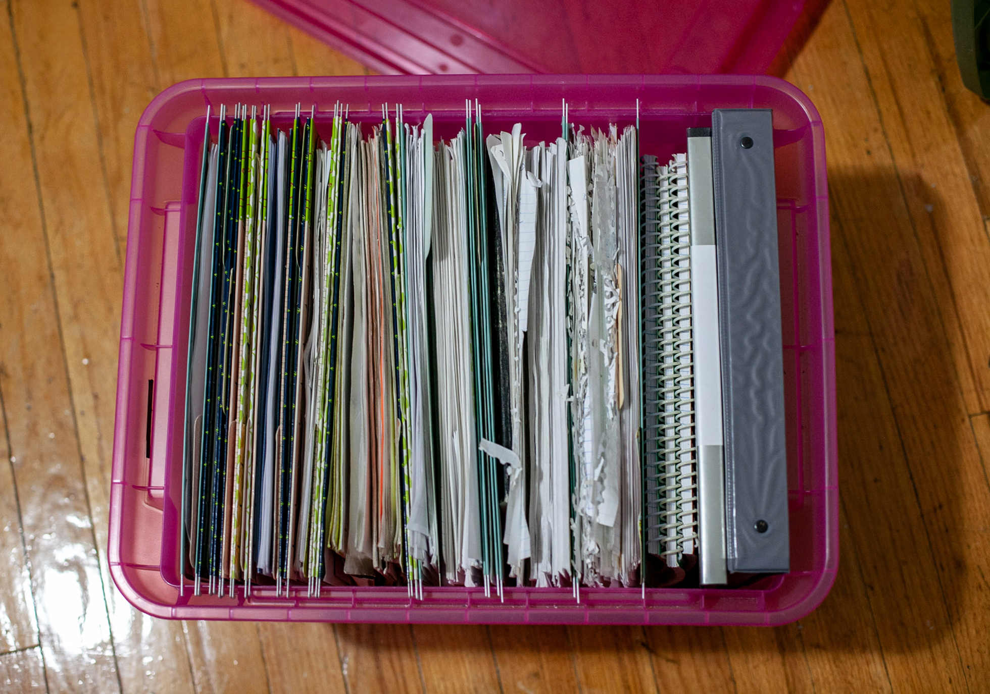 Clear pink plastic bin on wood floor overflowing with papers