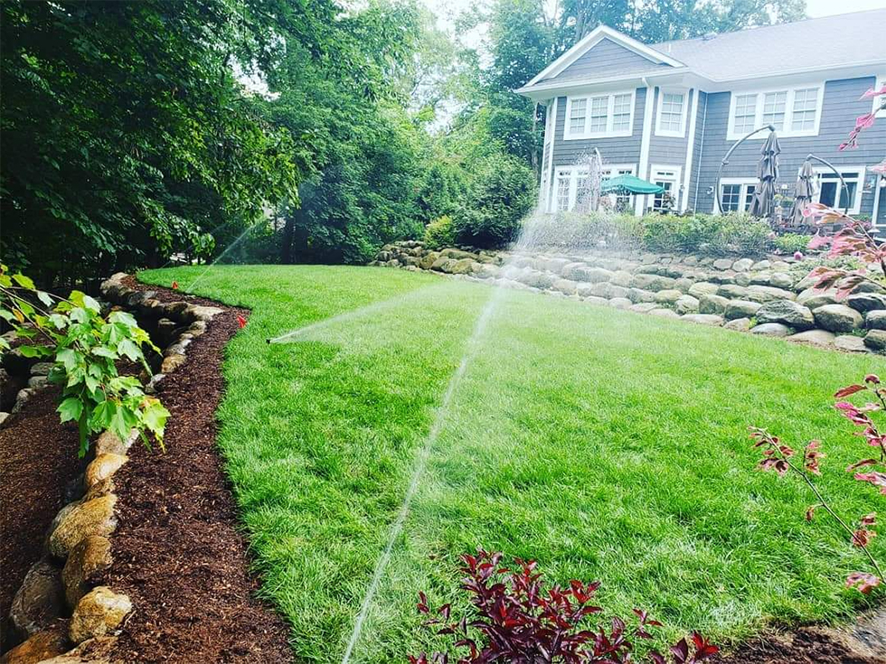 Three sprinklers behind house with stone retaining wall